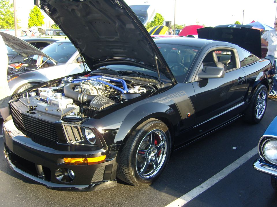 Black 2007 Ford Mustang with hood open, showing supercharger. Another car is parked to the left