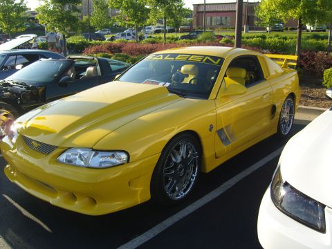 2007 Ford Mustang - A yellow Saleen Mustang is parked at a car show, a prominent hood scoop and custom chrome wheels.
