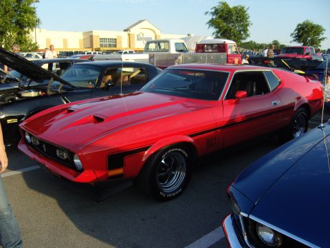 2007 Ford Mustang - A red 1971 Ford Mustang Mach 1 is parked next to a blue car, with other vehicles and a building in the background.