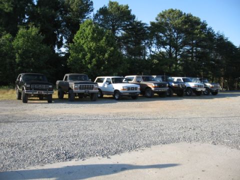 1978 Ford Bronco - A collection of Ford trucks and SUVs are lined up in a gravel lot under a clear sky.