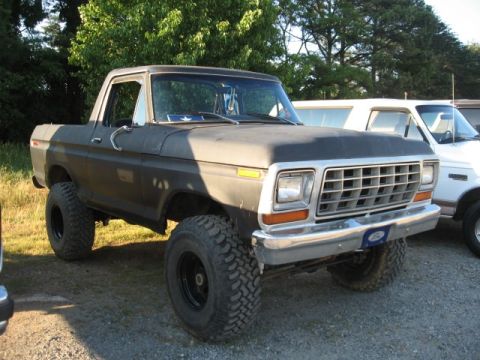 1978 Ford Bronco - A dark-colored, lifted Ford Bronco is parked outdoors next to a white SUV.
