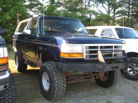 1978 Ford Bronco - Lifted blue Ford Bronco with aftermarket bumper and large tires, parked outdoors.