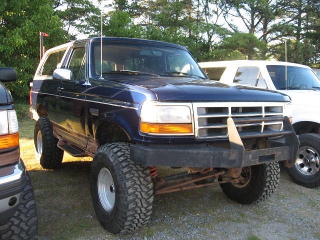 Blue Ford Bronco with lifted suspension and off-road tires parked next to a white SUV