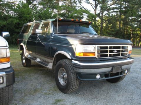 1978 Ford Bronco - A dark green SUV is parked next to a white vehicle, showing its front and side profile.