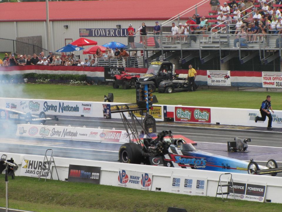 drag race with two dragsters on track, spectators in stands, and pit crew vehicles in background