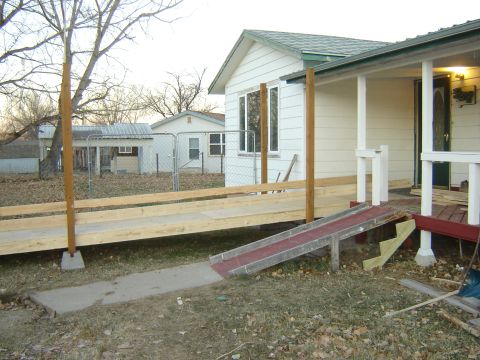 1984 Ford Mustang - A house features a newly constructed wooden ramp alongside an existing red ramp, with a chain-link fence in the background.