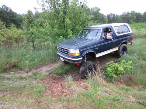 1992 Ford Bronco - 1992 Ford Bronco navigating an off-road trail with tall grass and trees surrounding it.