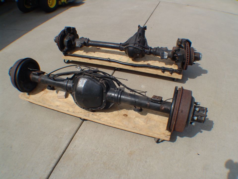 Two black vehicle rear axles on wooden dollies, one with drum brakes, the other with disc brakes