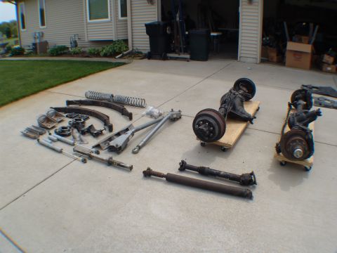 1996 Ford Bronco - Collection of vehicle parts, including axles and suspension components, displayed on a driveway.