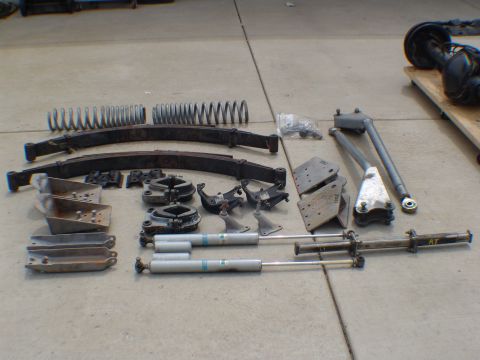 1996 Ford Bronco - Various suspension components are laid out on a concrete surface, including leaf springs, shocks, and mounting hardware.
