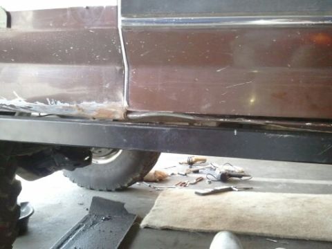 1982 Ford Bronco - The lower side panel of a brown vehicle displays significant rust and body filler, indicating repair work.