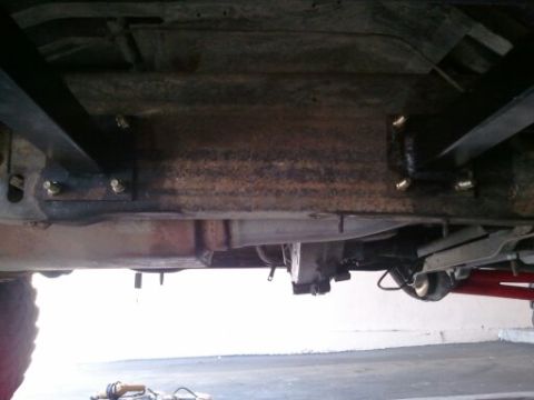 1982 Ford Bronco - The underside of a vehicle is shown, with focus on the frame and suspension parts, revealing signs of wear and tear.