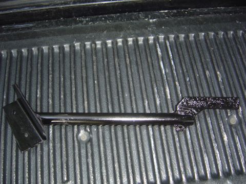 1986 Ford Bronco - A close-up view of a painted metal bracket, likely a vehicle part, placed on a textured surface.