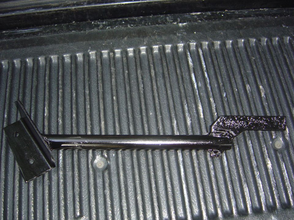 Black metal steering box bracket resting on a truck bed liner