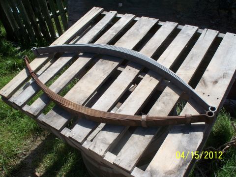 1990 Ford Bronco - Two leaf springs are displayed on wooden pallets, with one showing significant rust and the other appearing newer.