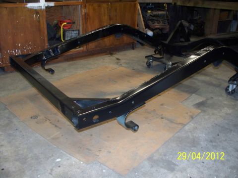 1990 Ford Bronco - A black vehicle frame is shown on casters, resting on cardboard in a workshop.