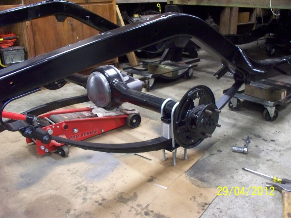 Black painted vehicle frame and rear axle assembly on a red jack and dollies