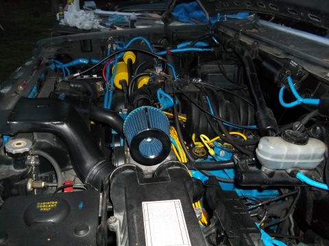 1989 Ford Bronco - Close-up view of a modified engine bay with custom blue and yellow wiring and components.