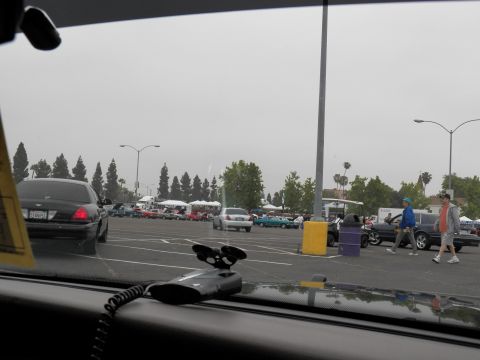 2003 Ford Crown Victoria - Pedestrians cross a wide event lot with vendor canopies seen past a black sedan's roofline.