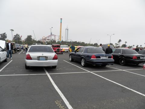 2003 Ford Crown Victoria - silver Mercury and dark Ford sedans share a show lot with coasters on the skyline.