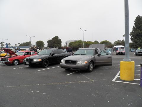 2003 Ford Crown Victoria - gray Crown Victoria with door open parks near a black push-bar sedan and red Mustang.