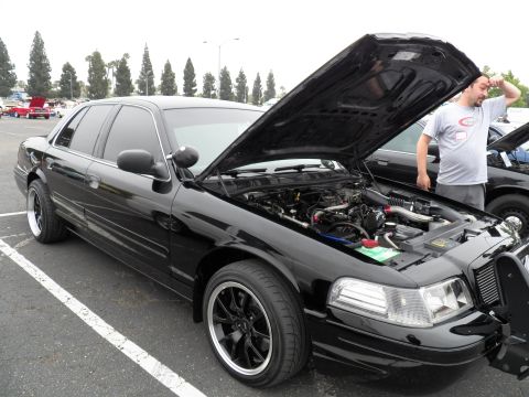 2003 Ford Crown Victoria - Black Crown Victoria with hood raised and dark wheels; a man inspects the engine bay.