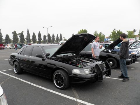 2003 Ford Crown Victoria - Black Crown Victoria displayed with hood up as two attendees converse in the parking lot.