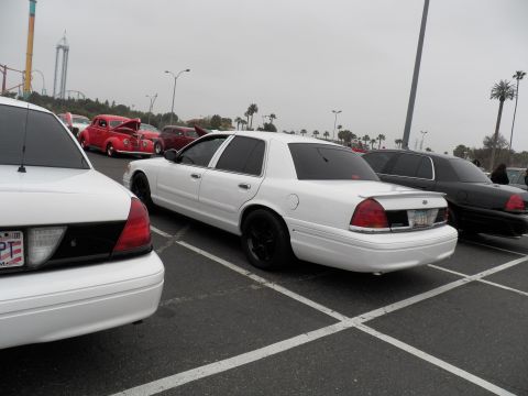 2003 Ford Crown Victoria - White Crown Victoria with dark wheels flanked by other sedans and a red hot rod in the lot.