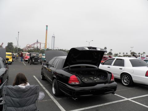 2003 Ford Crown Victoria - Rear view of a black full-size Ford sedan, trunk raised, parked near a roller coaster at an outdoor meet