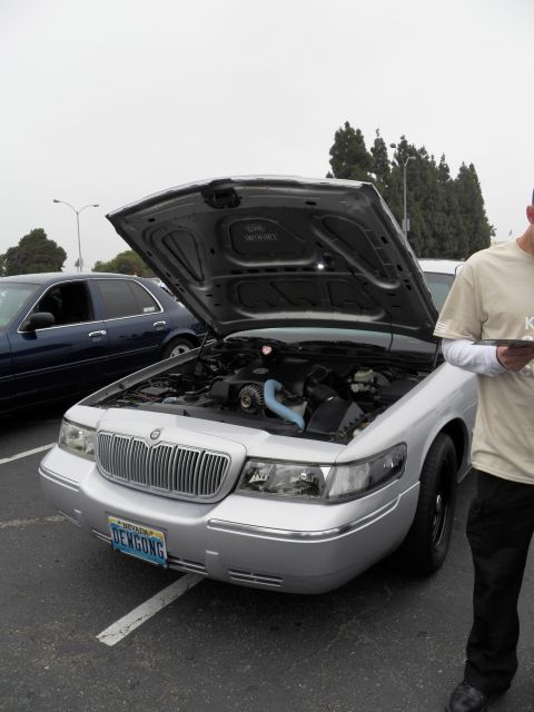 2003 Ford Crown Victoria - Front of a silver Mercury sedan with raised hood; owner stands at right holding paperwork