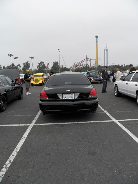 2003 Ford Crown Victoria - Rear of a black Crown Victoria sedan parked in a lot, roller coasters visible in the hazy background