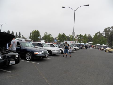 2003 Ford Crown Victoria - Lowered dark Ford sedan among parked vehicles; a man and child walk past tents in background