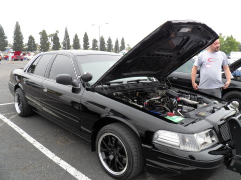 2003 Ford Crown Victoria - Side-front view of a lowered black Crown Vic, hood raised, person standing at the rear