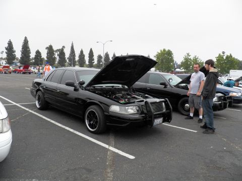 2003 Ford Crown Victoria - Side-front of a black Crown Vic with brush guard; two men converse at the right side