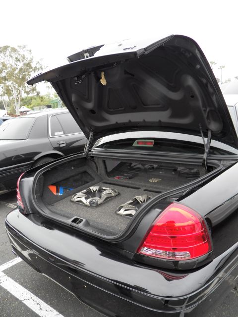 2003 Ford Crown Victoria - Rear quarter of black Crown Victoria, trunk raised to reveal subwoofer audio setup in carpeted floor