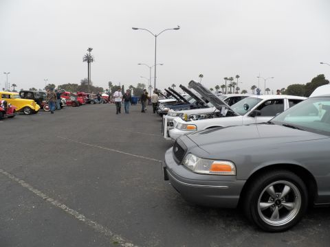 2003 Ford Crown Victoria - Gray Crown Victoria with five-spoke wheels nearest, lineup of hood-up sedans and vintage rods beyond