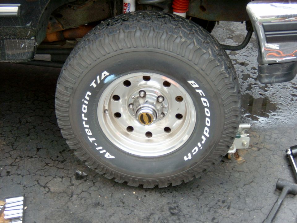 BFGoodrich All-Terrain T/A tire on chrome slotted wheel, lug studs bare, truck up in garage
