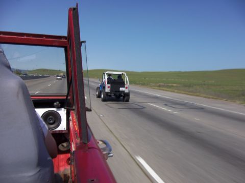 1968 Ford Bronco - Two Jeeps travel down a highway on a clear day, with green hills in the background.