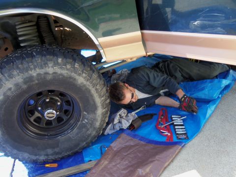 1968 Ford Bronco - A mechanic works on the undercarriage of a truck, surrounded by tools and a large tire.