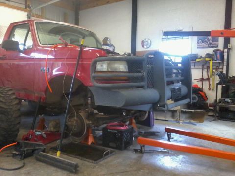1995 Ford F-150 - This red Ford F-150 is in a garage, lifted on jack stands with its front end exposed for work.