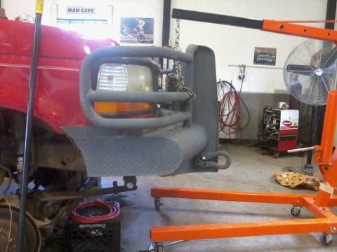 1995 Ford F-150 - A red truck's front end, equipped with a brush guard, is suspended by an engine hoist in a workshop.