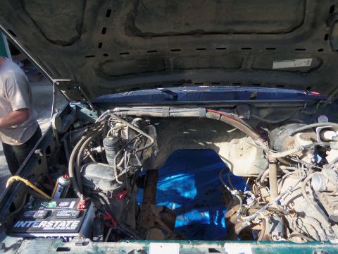 1968 Ford Bronco - The engine bay of a green vehicle is shown with the hood open, revealing various mechanical parts and a battery.