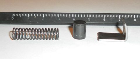 1985 Ford Bronco - Three small parts, including a spring, cylinder, and bracket, are shown next to a ruler for scale.
