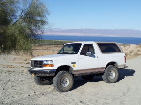 1996 Ford Bronco - This 1996 Ford Bronco is captured in a three-quarter front view, parked in a desert landscape with a lake and mountains visible.