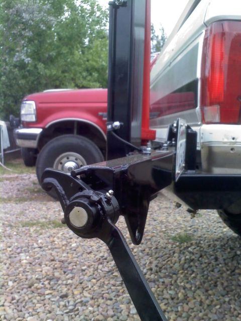 1996 Ford Bronco - Trailer hitch mechanism on a white vehicle, with a red Ford F-Series truck in the background.