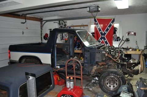 1986 Ford Bronco - A pickup truck is disassembled in a garage, with its engine compartment and front end completely removed.