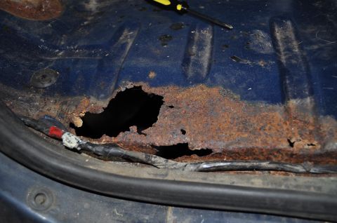1986 Ford Bronco - Significant rust has eaten through the floor pan, revealing a hole and exposed wiring.