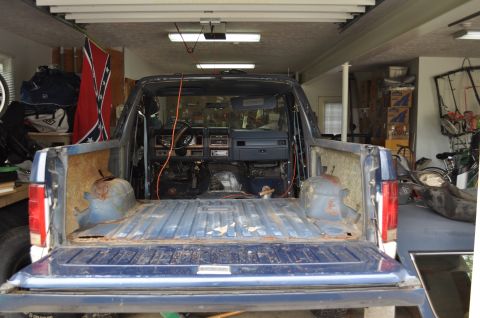 1986 Ford Bronco - Disassembled blue pickup truck interior, with dashboard and empty bed visible. A Confederate flag hangs in the background.