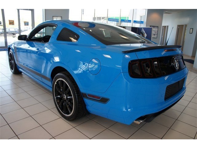Blue Ford Mustang with black spoiler and racing stripes, viewed from rear three-quarter angle