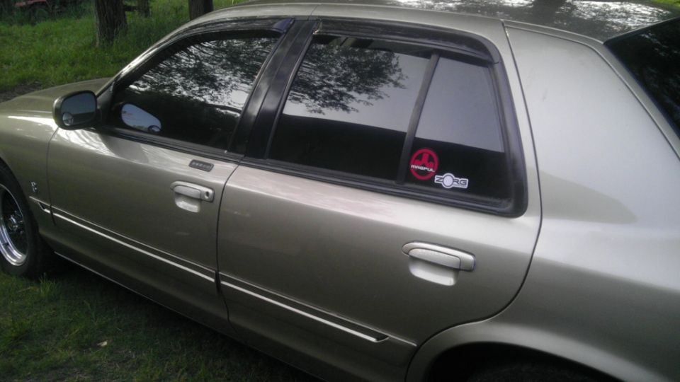 tan sedan parked on grass, side view. Has a sticker on rear window